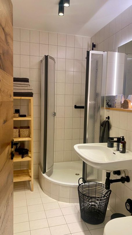 Klein, modernes Badezimmer mit Duschkabine, Waschbecken und Holzregal. 