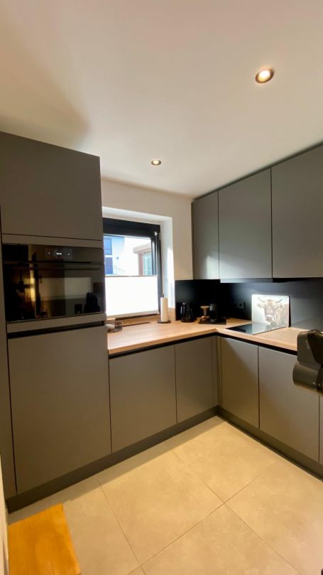 Moderne, minimalistische Küche mit grauen Schränken und Holzarbeitsplatte.