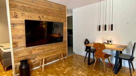 Holzwand mit TV, Esstisch und Stühlen in modernem Wohnbereich. Ferienwohnung Schleching
